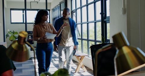 African american coworkers collaborating while walking through sunlit open-plan office