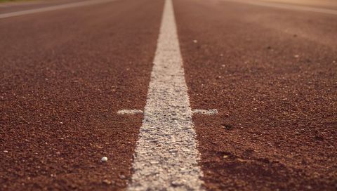 Running white center line along sunlit red track during golden hour with textured surface