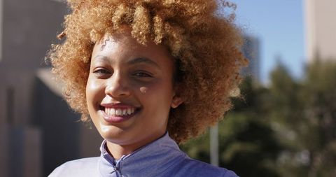Smiling African American woman wearing lavender athletic top posing in sunny urban park