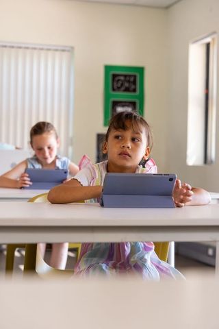 Young girls using tablets in bright classroom, pastel dress, focused digital learning
