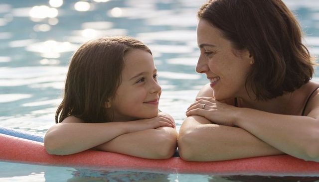 Mother and daughter relaxing on pool noodle smiling and bonding in sunlit swim