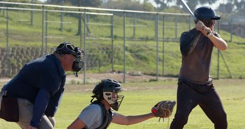 Batter preparing to swing while catcher reaching for low pitch and umpire watching