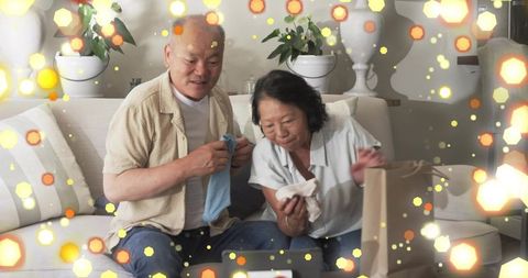 Mature chinese couple unboxing gifts on couch inspecting clothes in cozy living room