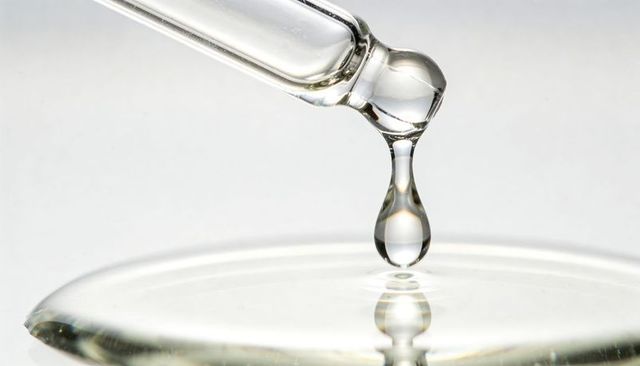 Glass pipette releasing single droplet over reflective dish, macro lab liquid close-up