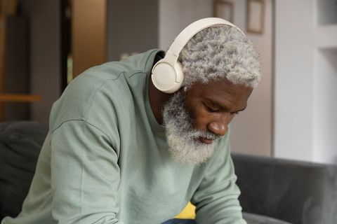 Senior african american man listening with headphones on modern living room sofa