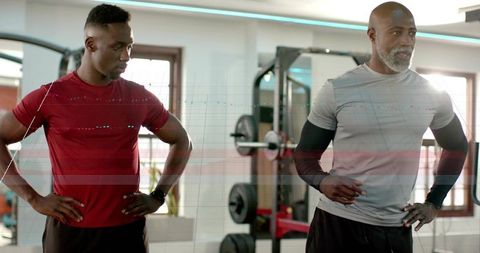 Training partners pausing midworkout in modern gym with barbell and mirror reflections