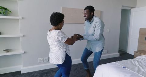 African American couple dancing joyfully while holding hands in bright modern bedroom