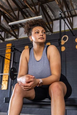 African american woman resting on workout bench wearing smartwatch, showing determination