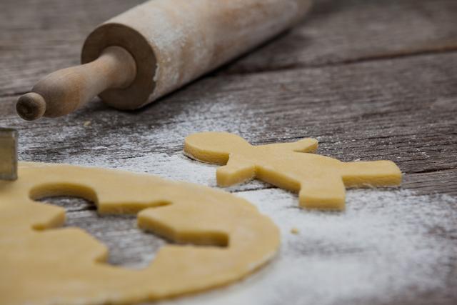 Gingerbread dough with a cut-out shape and a rolling pin on a rustic wooden surface. Ideal for holiday baking themes, cooking blogs, festive recipe illustrations, and kitchen-related content.