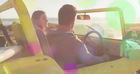 Driving couple in yellow dune buggy along coastal sunset with surfboard, lens flare