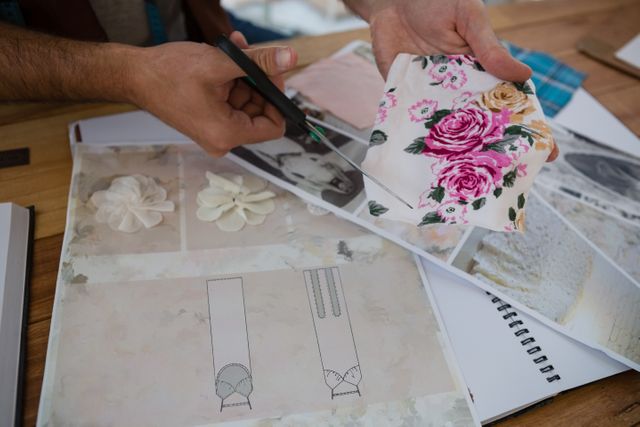 Cropped hands of designer cutting papers at table in studio