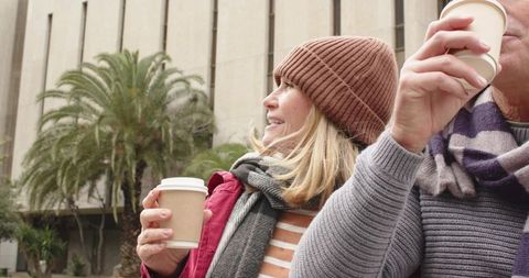 Senior couple enjoying morning coffee on city sidewalk in cozy winter apparel