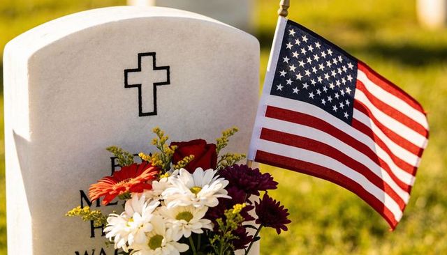 White marble military headstone catching golden light with bouquet and american flag