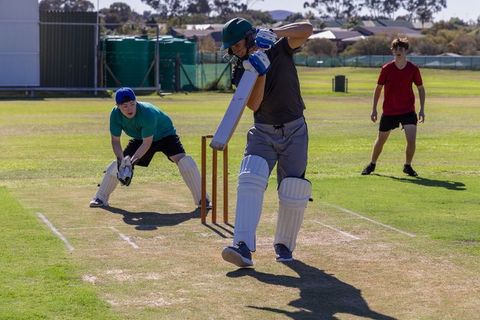 Youth cricket match on suburban pitch batter defending wicket wearing pads and helmet