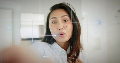 Mid adult asian woman speaking and touching shirt while recording smartphone selfie closeup portrait