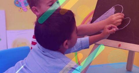 Preschool boys drawing chalk heart on easel, collaborating in colorful classroom