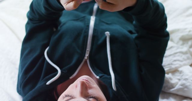 Person Browsing Smartphone While Lying on Bed in Casual Hoodie - Download Free Stock Images Pikwizard.com