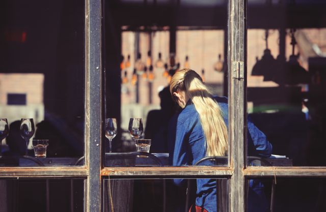 Waitress in a relaxed modern urban cafe, seen from the rear, serves at a table under soft lighting with glasses and tableware. Ideal for illustrating themes of service industry work, hospitality, business environments, and daily work routines.