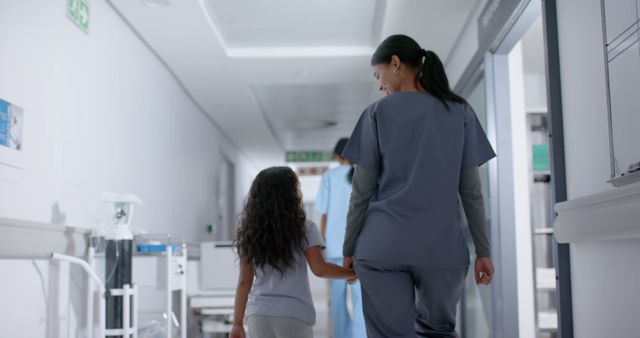 Biracial girl and female surgeon walking and holding hands in hospital. Medicine, healthcare, childhood and hospital, unaltered.
