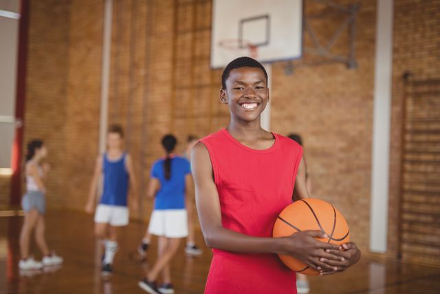 Portrait of smiling school boy holding a basketball while team playing in background