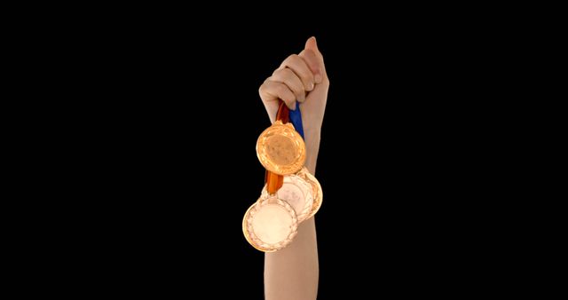 Smooth and isolated black background accentuates the hand holding three gold medals. Ideal for use in layouts promoting sports achievements, motivational content such as athleticism, excellence, and success in general. Can be effectively used for themes of winning in competitions, awards, and personal achievements in sports or other fields.