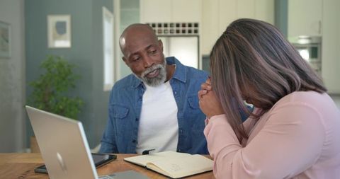 Diverse senior couple managing finances and discussing bills while using laptop at home
