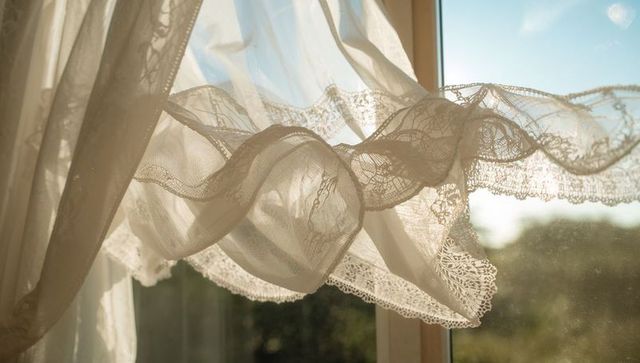 Sunlit sheer lace curtain billowing at window with scalloped trim and warm backlight