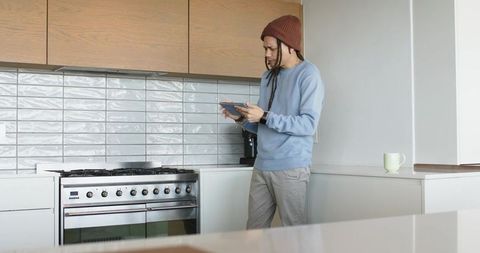 Mid adult african american man holding tablet in modern kitchen near range and coffee maker
