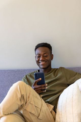 Relaxed young man using smartphone while reclining on sofa in minimalist living room