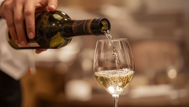 Pouring white wine into stemmed glass with bubbles and warm bokeh ambience