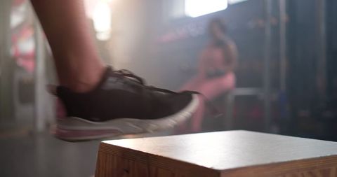 Diverse women jumping onto wooden plyo box in gym, close-up black sneaker motion