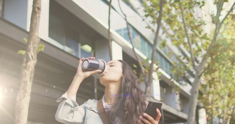 Woman Drinking Coffee While Using Smartphone on City Street
