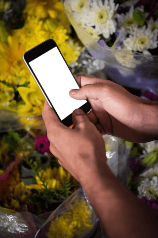 Hands holding mobile phone with transparent screen amidst colorful flowers