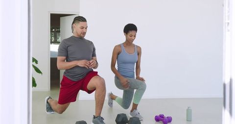 Diverse athletes lunging with dumbbells in home gym