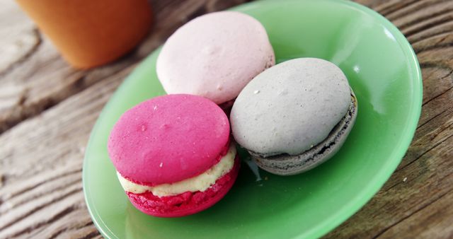 Assorted macarons featured on a vibrant green plate, placed on a rustic wooden table. Ideal for use in advertising gourmet baked goods, baking blogs, food-related websites, or as a decorative image for kitchens and culinary spaces.
