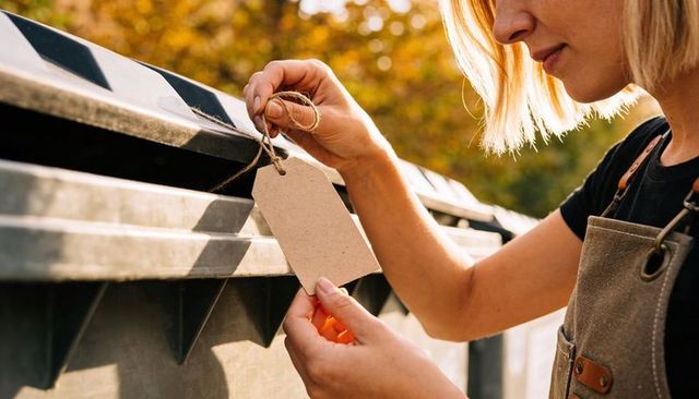 Tying twine tag to recycling bin lid by woman wearing canvas apron at golden hour