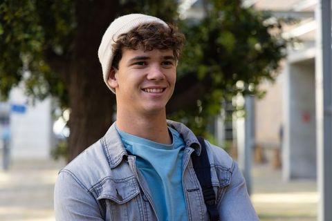 Smiling teenage student standing on campus wearing beanie and denim jacket
