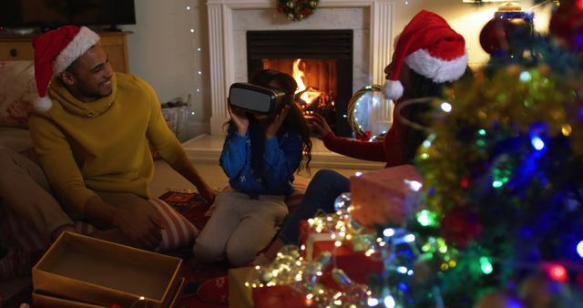 Family enjoying Christmas night near cozy fireplace. Child wearing VR headset experiencing virtual reality while parents watch joyfully. Presents and festive decorations. Perfect for advertisements, blogs on holiday traditions, technology influence in holidays, or family-centered promotions.