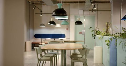Modern coworking space featuring communal table, pastel pendant lights and indoor greenery