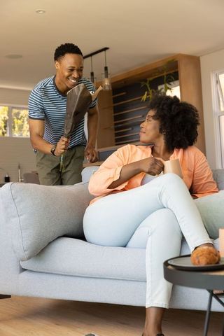 African american man surprising partner with wrapped bouquet in cozy living room