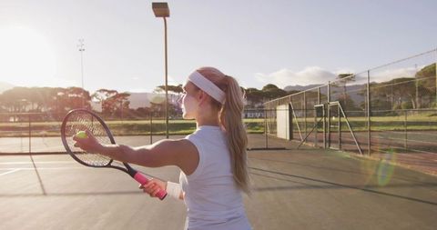Young Female Tennis Player Preparing Powerful Serve on Outdoor Hard Court at Sunset