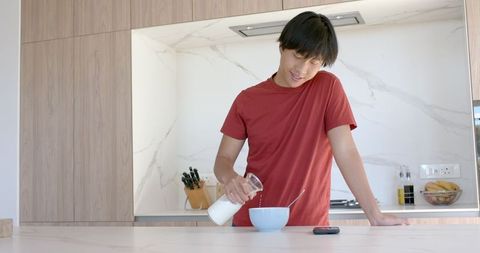 Young man pouring milk for breakfast in modern kitchen