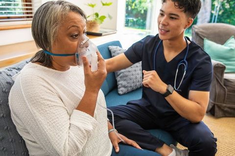 Senior Woman with Oxygen Mask Receiving Nurse Care at Home