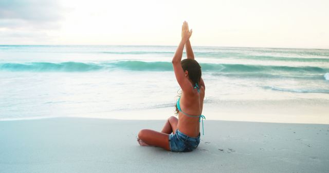 Woman practicing yoga on tranquil beach at sunrise, facing ocean waves. Ideal for wellness advertisements, fitness blogs, and relaxation retreat promotions.