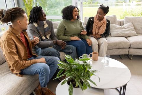 Friends laughing and chatting on sectional sofa in sunlit modern living room with plants