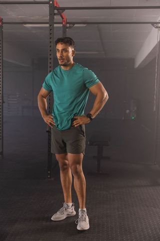 Man resting after intense strength workout wearing smartwatch and shorts in functional gym
