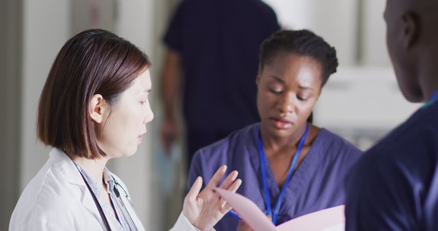 Doctor discussing patient care with nurses in a hospital corridor. Useful for illustrating medical teamwork, healthcare environments, professional consultations, and healthcare services in a clinical setting.