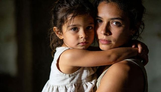 Mother holding daughter in protective embrace, intimate portrait with moody lighting
