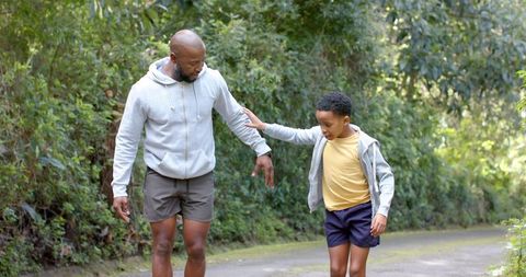 African american father and son walking on forest trail bonding outdoors