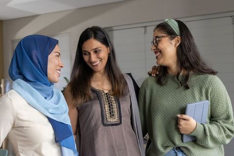 Diverse women smiling and bonding while chatting in cozy lounge holding tablet